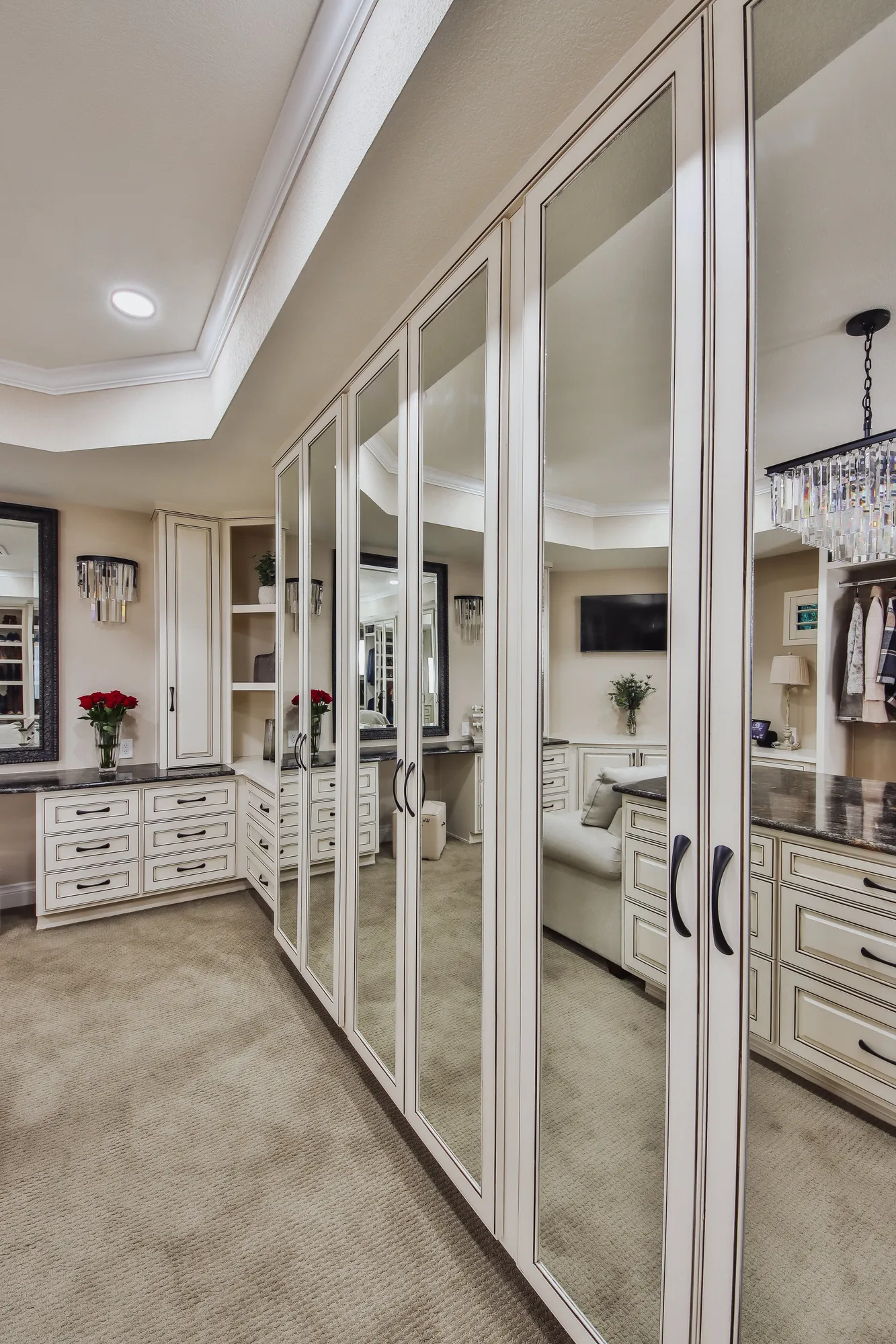 A bedroom with cream-colored cabinetry, mirrored closet doors, beige carpet, and various decorations including a bouquet of red roses and framed artwork.