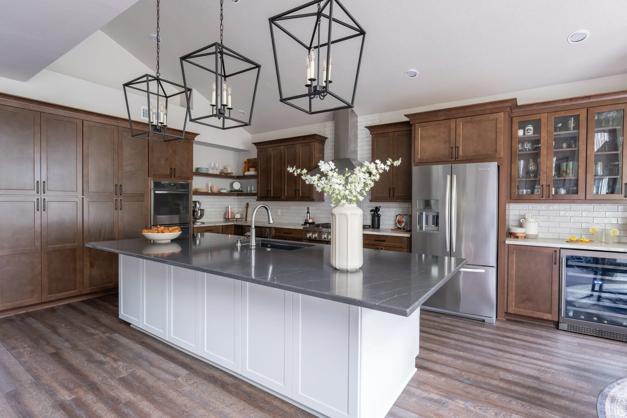After: white kitchen island with a dark countertop under lantern pendants, wood cabinets behind