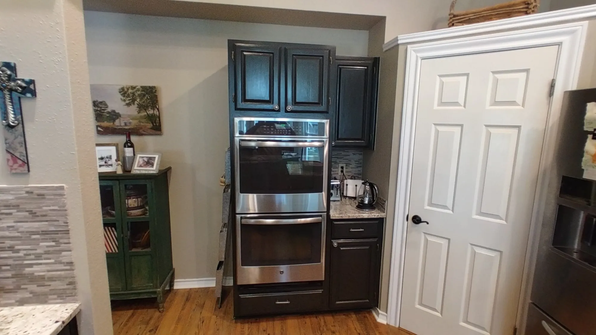 Before: dark cabinets with a double wall oven beside a white pantry door