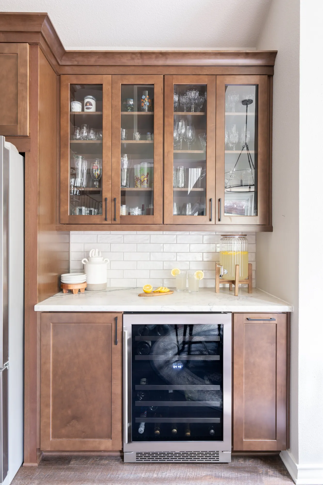 After: wood bar cabinet with glass doors, white subway tile and a wine fridge
