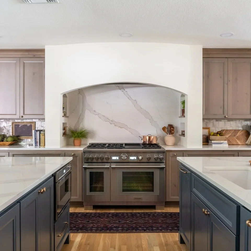 Kitchen with taupe cabinetry, a range under a marble hood and a navy island
