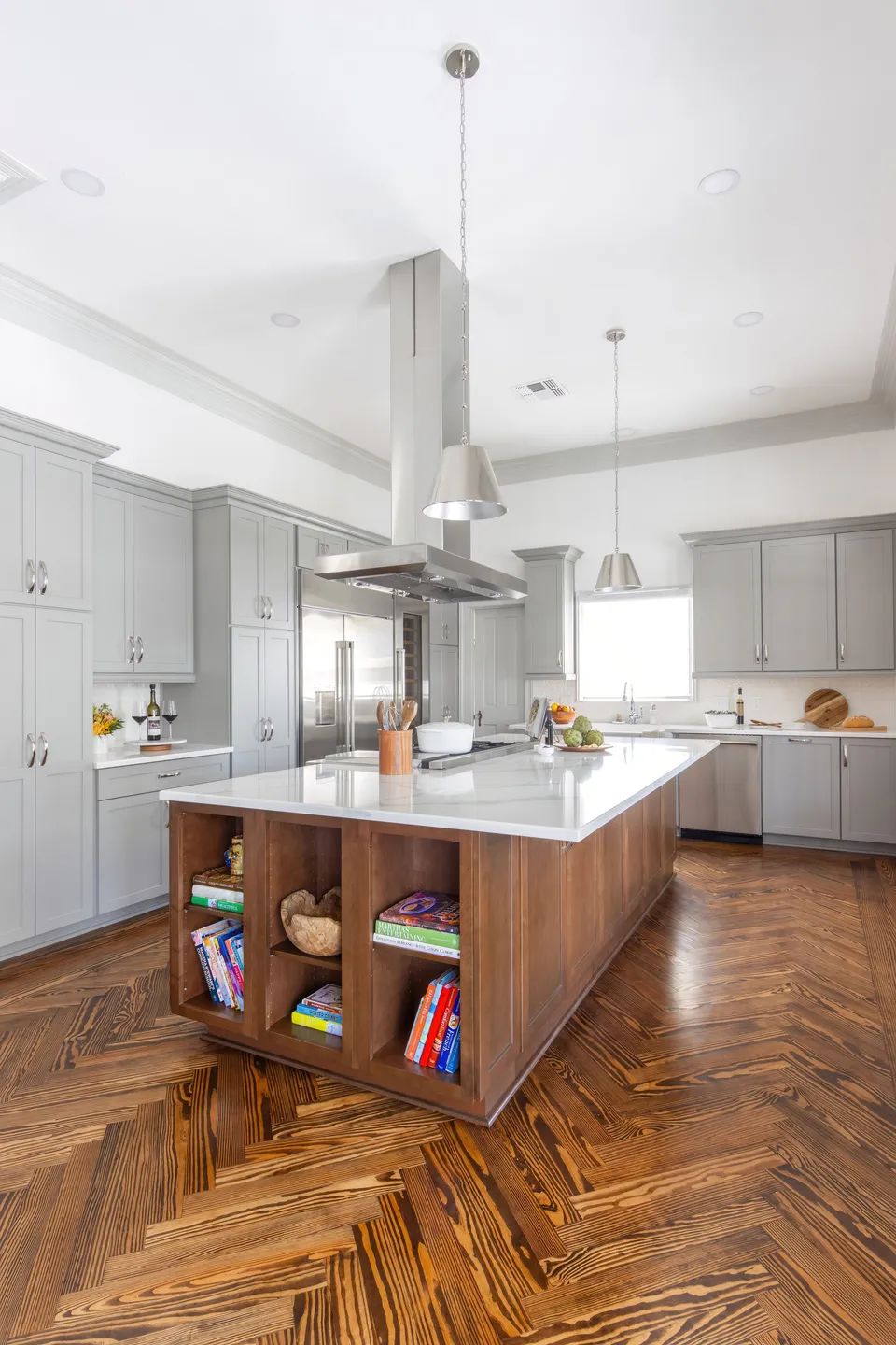 Modern kitchen with gray cabinets, white countertops, and a wooden island with open shelving, hardwood floor, pendant lights, and stainless steel appliances.