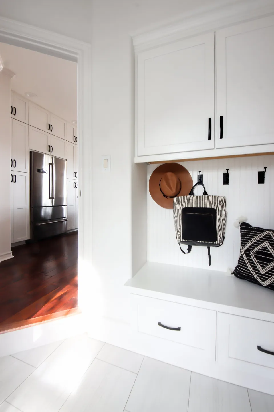 Entryway with white built-in storage, black hooks, a striped bag, a brown hat, and a cushion with a black and white design.