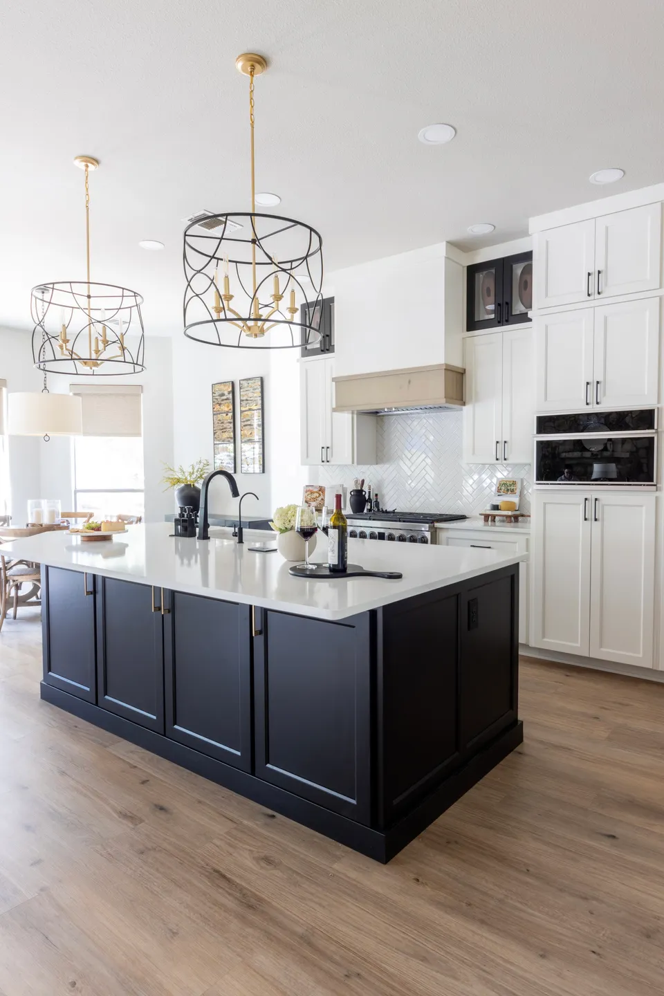 Modern kitchen with black island, white cabinets, and gold chandelier lighting fixtures.